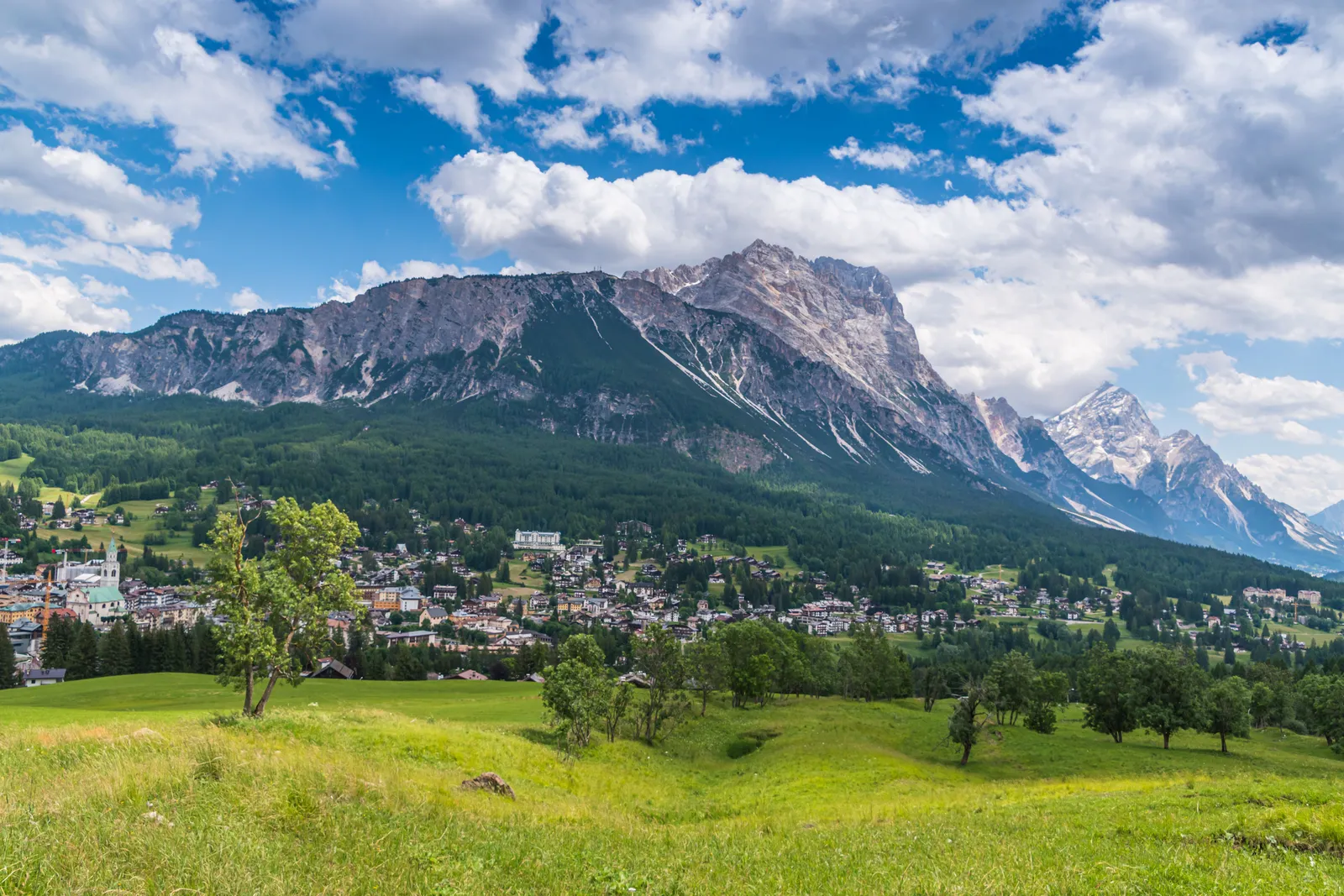 A cosy alpine village with wooden chalets and church spire below snow-dusted Dolomite peaks