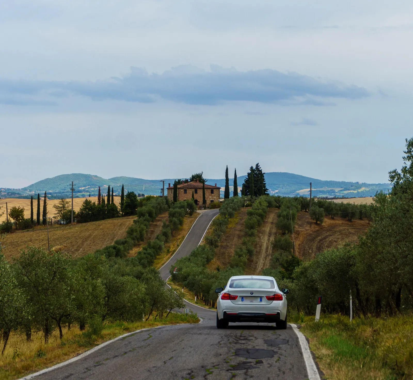 A car on a winding country road between cypress trees in the Tuscan countryside, Italy
